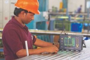 A man in an orange hard hat working on a computer.